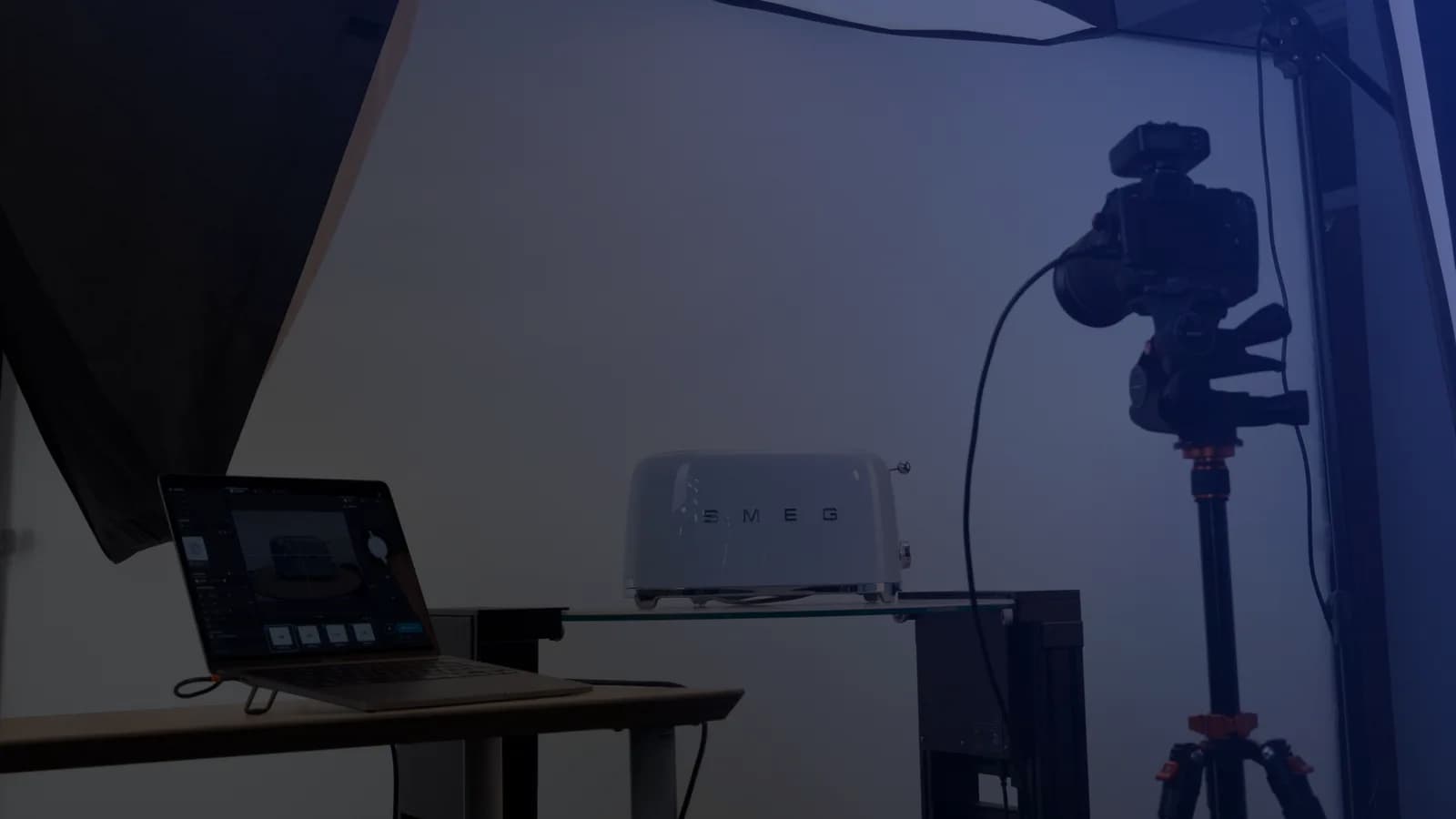 Set de fotografía de producto con tethering: un portátil con el software de captura junto a una cámara en trípode y un producto sobre una balda de cristal